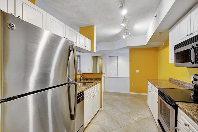 kitchen with track lighting, white cabinetry, appliances with stainless steel finishes, dark stone countertops, and sink