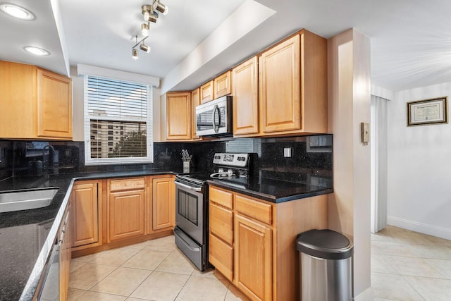 kitchen featuring stainless steel appliances, dark stone countertops, tasteful backsplash, sink, and light tile patterned flooring