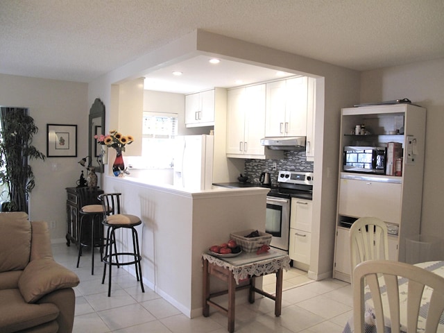 kitchen featuring kitchen peninsula, a textured ceiling, stainless steel appliances, a breakfast bar, and white cabinets