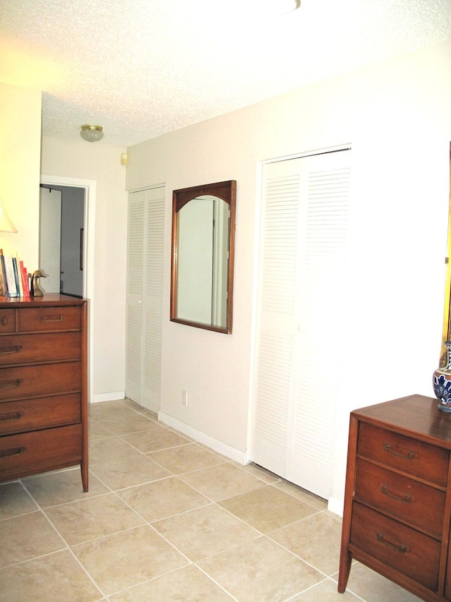 bedroom featuring a textured ceiling, light tile patterned flooring, and multiple closets