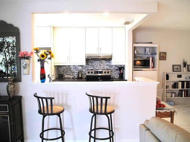 kitchen with stainless steel appliances, white cabinets, tasteful backsplash, and a kitchen bar