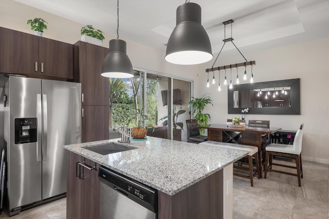 kitchen with a kitchen island with sink, appliances with stainless steel finishes, light stone countertops, sink, and decorative light fixtures