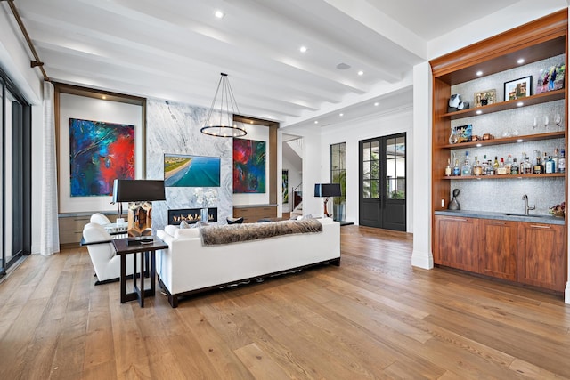 living room featuring a premium fireplace, light wood-type flooring, wet bar, and beam ceiling