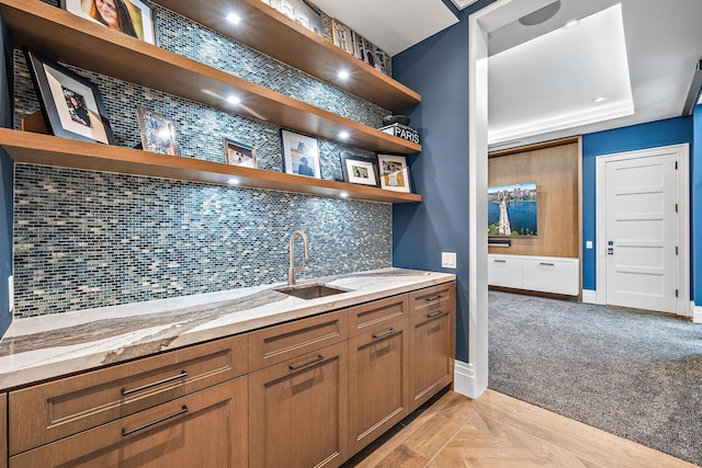 kitchen with light parquet flooring, light stone countertops, sink, and backsplash