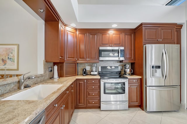 kitchen with light tile patterned floors, stainless steel appliances, decorative backsplash, light stone countertops, and sink