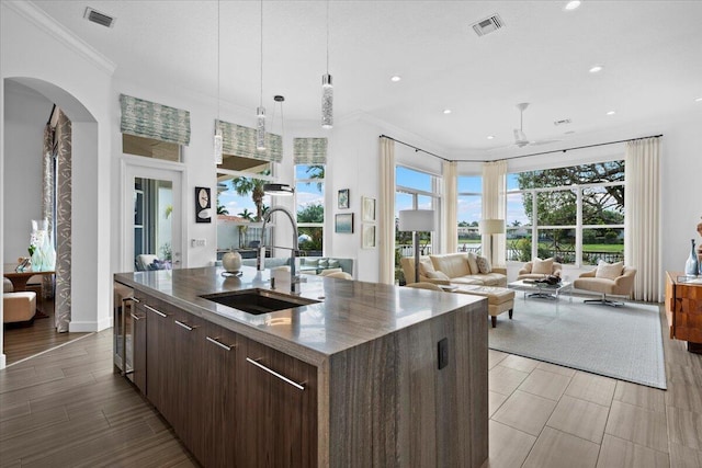 kitchen featuring dark brown cabinetry, sink, crown molding, ceiling fan, and a kitchen island with sink