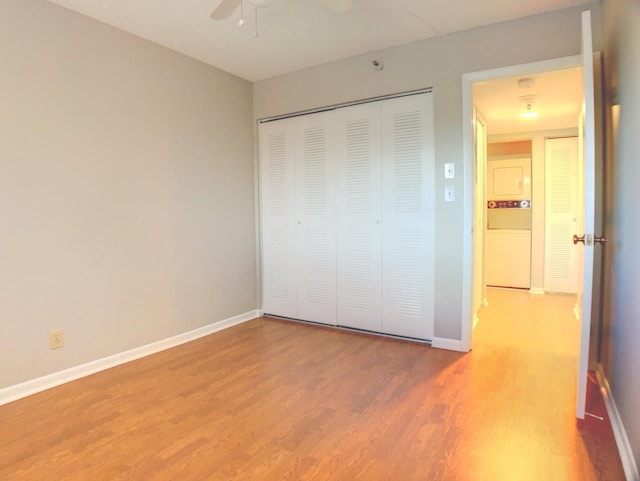 unfurnished bedroom with ceiling fan, stacked washer and dryer, a closet, and hardwood / wood-style flooring