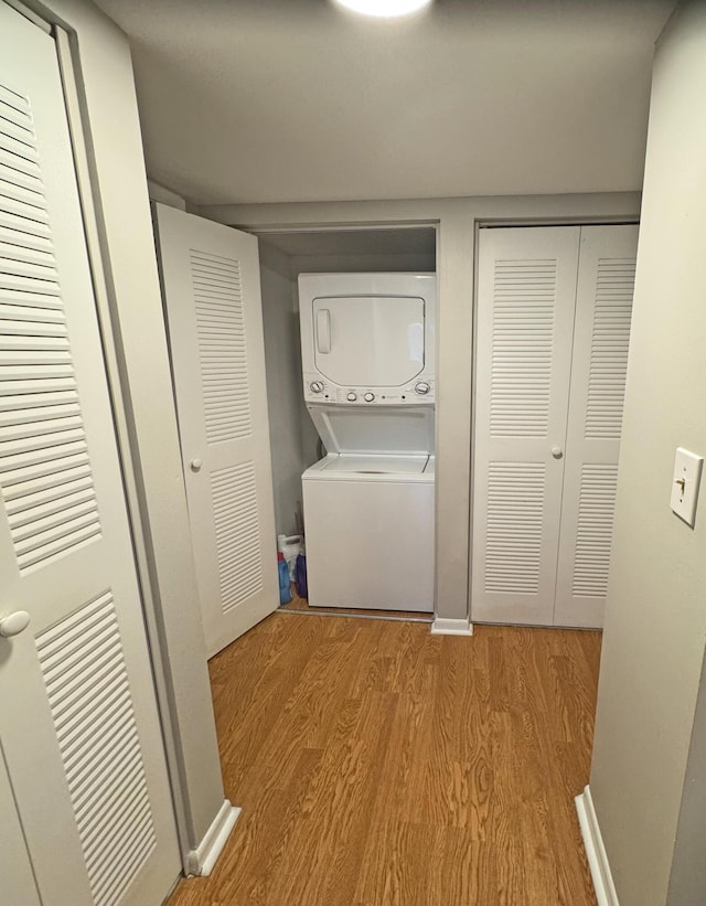 washroom with stacked washer and dryer and light hardwood / wood-style flooring