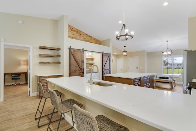 kitchen featuring decorative light fixtures, a barn door, sink, an inviting chandelier, and an island with sink