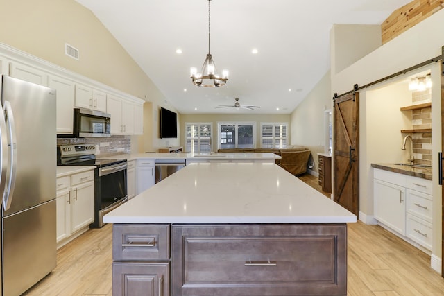 kitchen with ceiling fan, a barn door, decorative backsplash, stainless steel appliances, and white cabinets