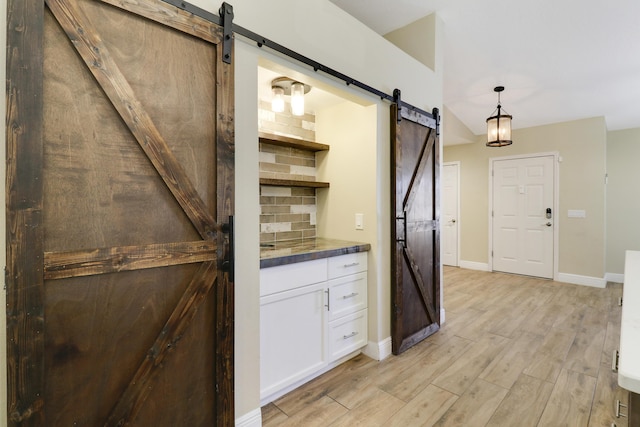 kitchen with pendant lighting, a barn door, white cabinets, and backsplash