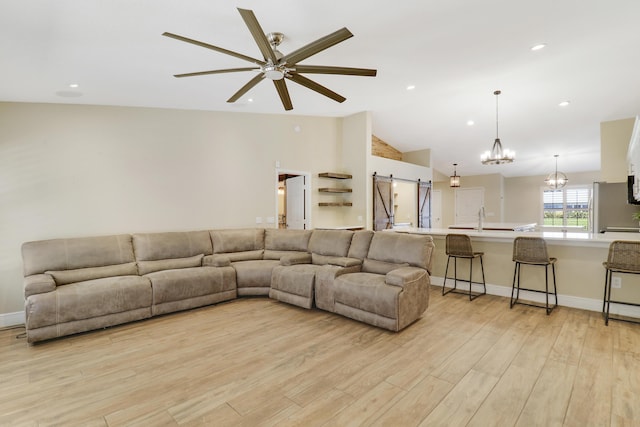 living room with ceiling fan with notable chandelier, lofted ceiling, light hardwood / wood-style floors, sink, and a barn door