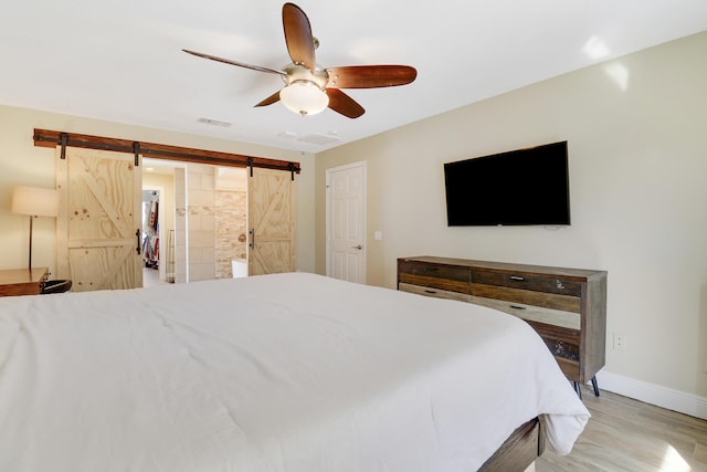 bedroom featuring ceiling fan, ensuite bath, a barn door, and light wood-type flooring