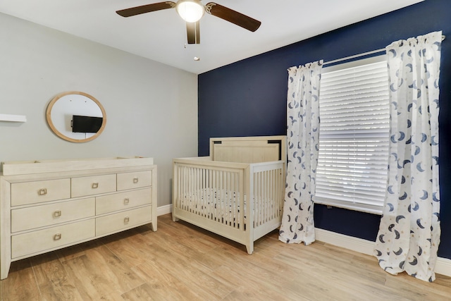 bedroom featuring ceiling fan, a crib, and light hardwood / wood-style flooring