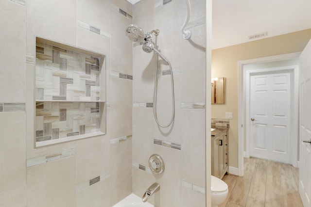 full bathroom with wood-type flooring, tiled shower / bath combo, vanity, and toilet