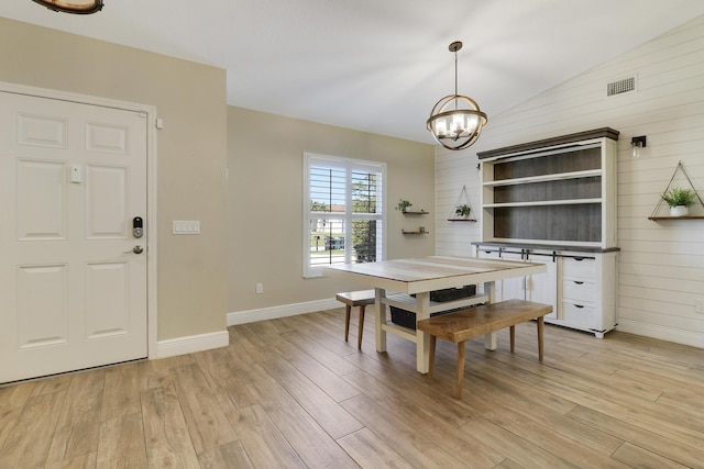 dining room with lofted ceiling, light hardwood / wood-style floors, wood walls, and a notable chandelier