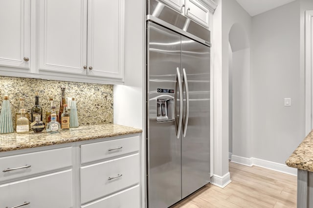 kitchen with white cabinetry, backsplash, light stone countertops, and stainless steel built in fridge