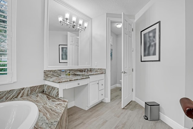 bathroom featuring a chandelier, vanity, toilet, a bath, and a textured ceiling