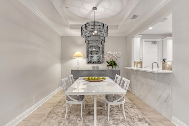 dining room with a chandelier, ornamental molding, a raised ceiling, and light hardwood / wood-style flooring