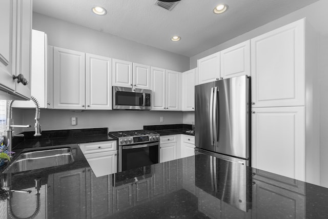 kitchen featuring sink, stainless steel appliances, a textured ceiling, white cabinets, and dark stone counters