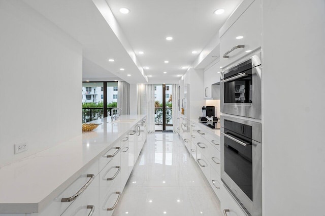 kitchen featuring light stone countertops, white cabinetry, sink, and oven