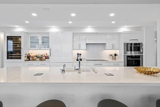 kitchen with light stone countertops, double oven, white cabinets, and sink