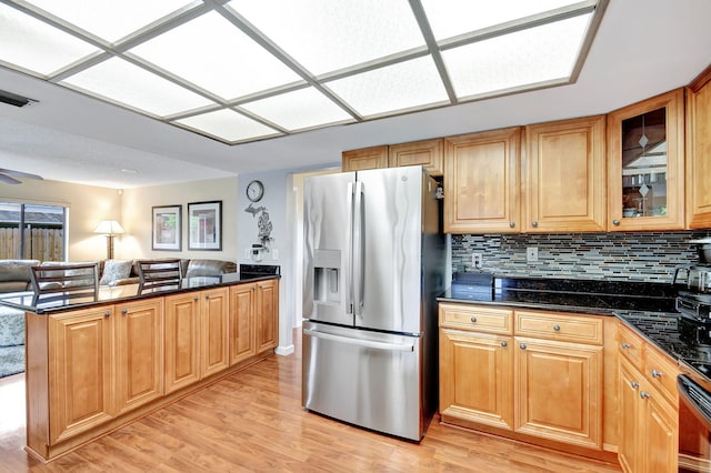 kitchen with dark stone counters, decorative backsplash, light hardwood / wood-style floors, stainless steel fridge with ice dispenser, and kitchen peninsula