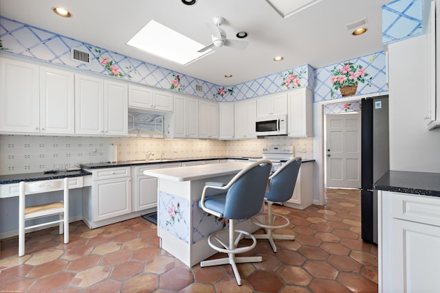 kitchen with ceiling fan, sink, white cabinets, a kitchen bar, and a skylight