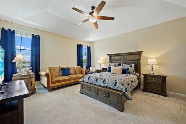 bedroom with ceiling fan, a tray ceiling, and light carpet