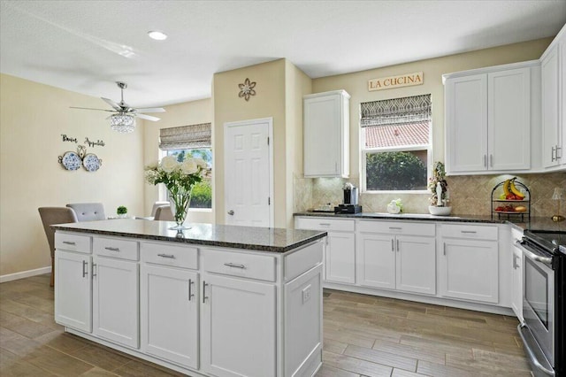 kitchen featuring white cabinets, stainless steel range with electric stovetop, a center island, a healthy amount of sunlight, and light wood-type flooring