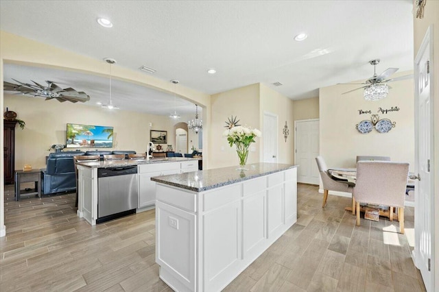 kitchen featuring stone counters, white cabinetry, dishwasher, sink, and an island with sink