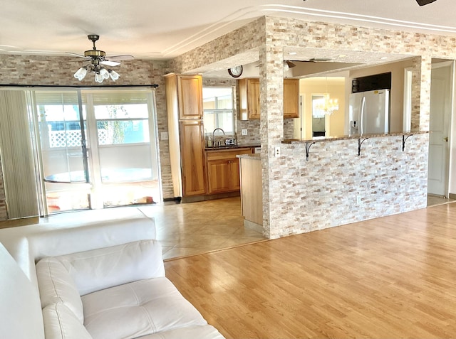 kitchen featuring stainless steel refrigerator with ice dispenser, a sink, ceiling fan with notable chandelier, light wood finished floors, and ornate columns