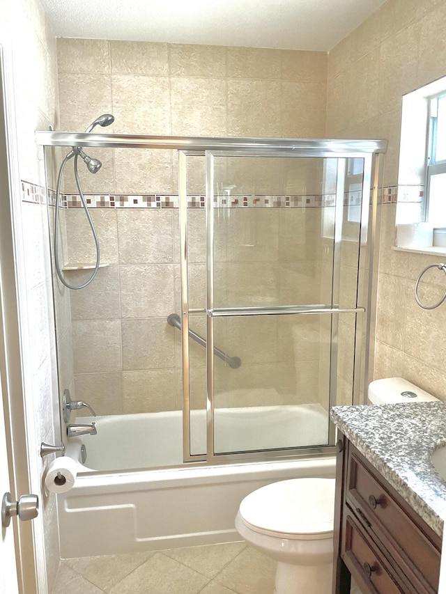 full bathroom with shower / bath combination with glass door, tile patterned flooring, vanity, tile walls, and toilet