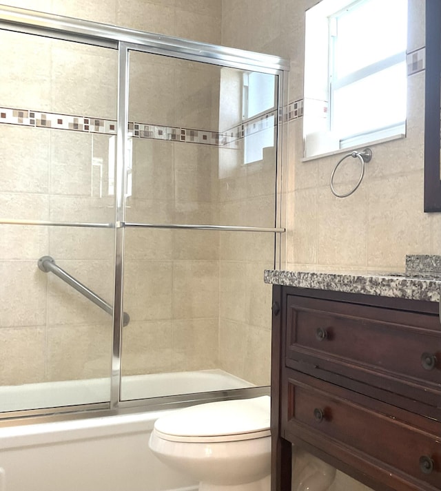 full bathroom with combined bath / shower with glass door, vanity, and toilet