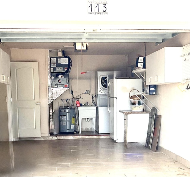 garage featuring freestanding refrigerator, stacked washer / drying machine, a sink, and electric water heater
