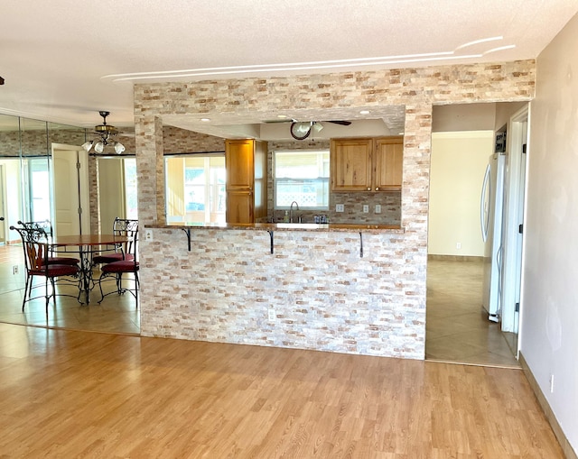 kitchen featuring light hardwood / wood-style floors, kitchen peninsula, a kitchen bar, fridge, and sink