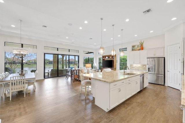 kitchen with pendant lighting, sink, appliances with stainless steel finishes, white cabinetry, and an island with sink