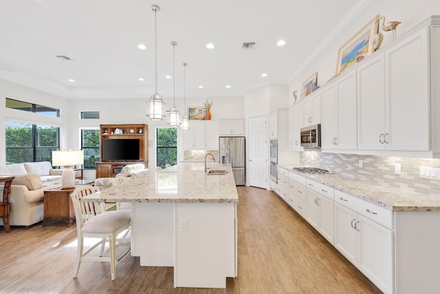 kitchen featuring decorative light fixtures, sink, white cabinets, stainless steel appliances, and a spacious island