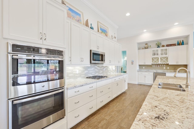 kitchen with white cabinetry, stainless steel appliances, sink, and light stone counters