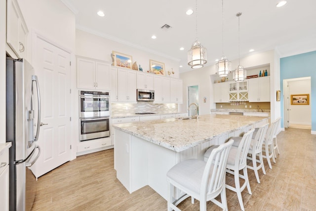 kitchen with white cabinetry, light stone counters, a center island with sink, appliances with stainless steel finishes, and pendant lighting