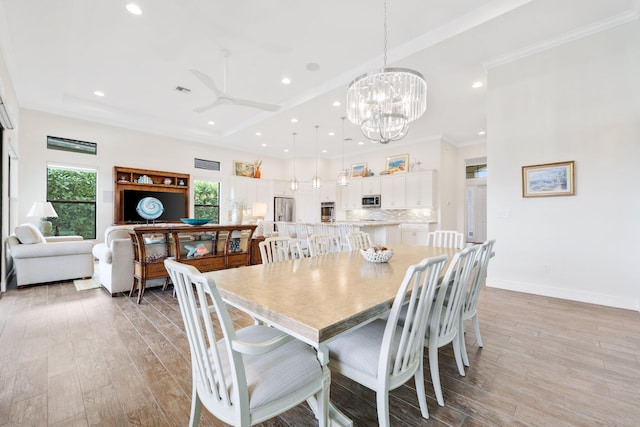 dining space with a tray ceiling, light hardwood / wood-style flooring, ornamental molding, and ceiling fan with notable chandelier