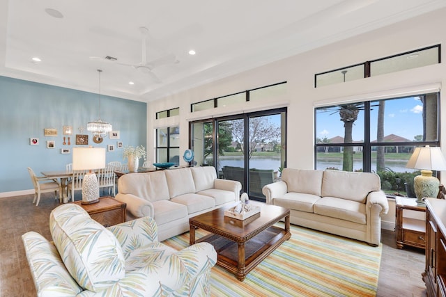 living room featuring a water view, a raised ceiling, ceiling fan with notable chandelier, and light hardwood / wood-style flooring