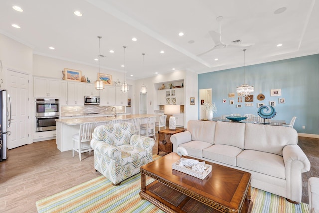 living room featuring sink, ceiling fan with notable chandelier, light hardwood / wood-style floors, and a raised ceiling