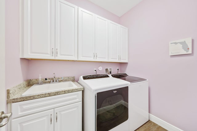 laundry area with sink, washing machine and dryer, cabinets, and light wood-type flooring