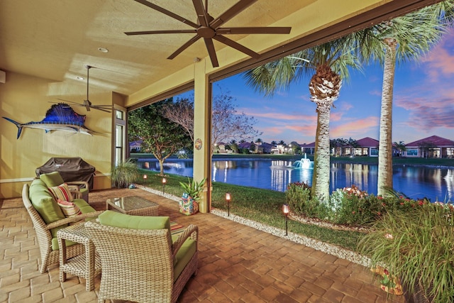 patio terrace at dusk featuring a grill, ceiling fan, and a water view