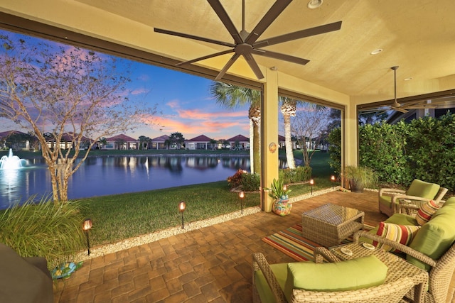 patio terrace at dusk with a water view, ceiling fan, and an outdoor hangout area