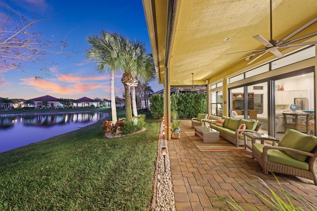 patio terrace at dusk with a water view, an outdoor hangout area, a yard, and ceiling fan