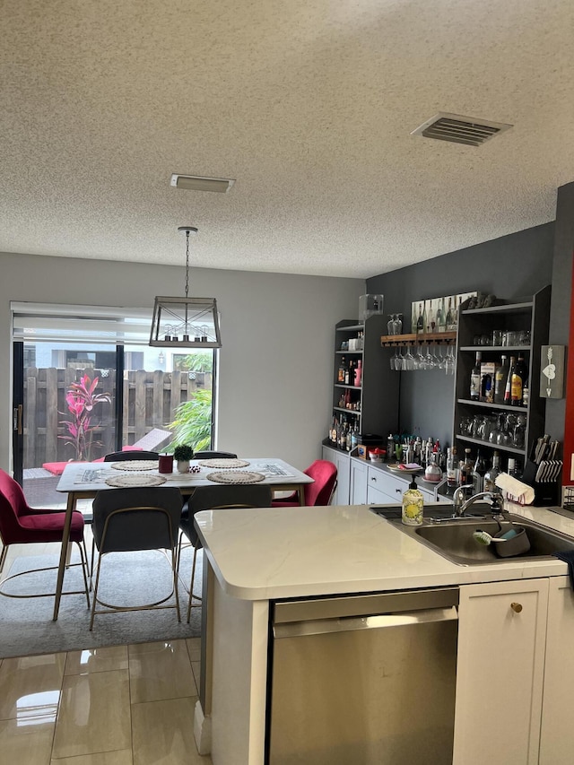 kitchen featuring a textured ceiling, white cabinetry, stainless steel dishwasher, and hanging light fixtures