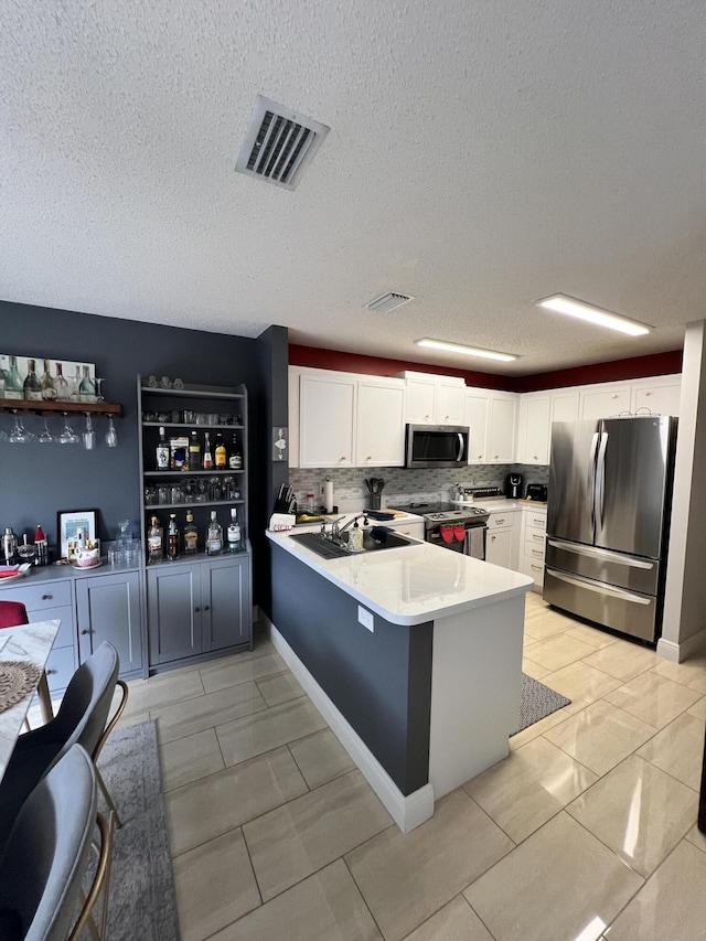 kitchen with a textured ceiling, white cabinets, appliances with stainless steel finishes, decorative backsplash, and kitchen peninsula