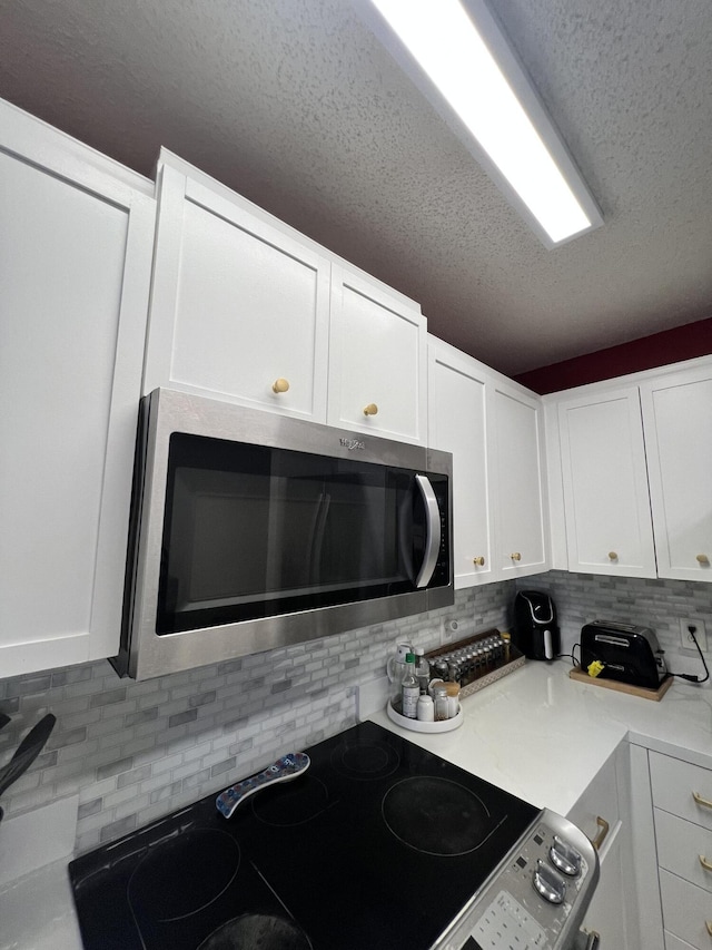 kitchen featuring decorative backsplash, a textured ceiling, stainless steel appliances, and white cabinetry